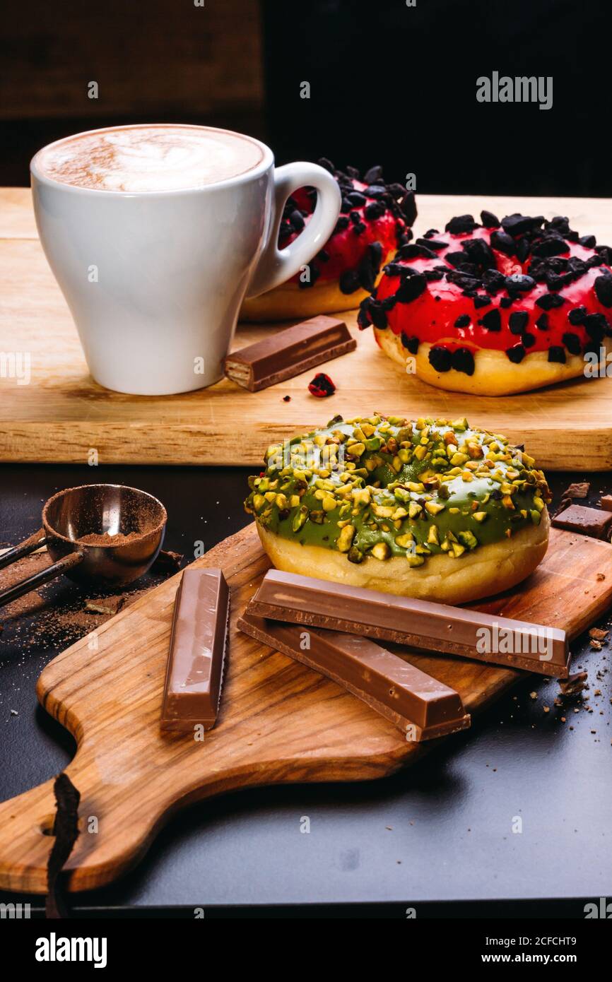 Verschiedene leckere Donuts mit Glasur und Toppings mit Schokolade zusammengesetzt Bars und eine Tasse Kaffee auf Holzbrettern Stockfoto