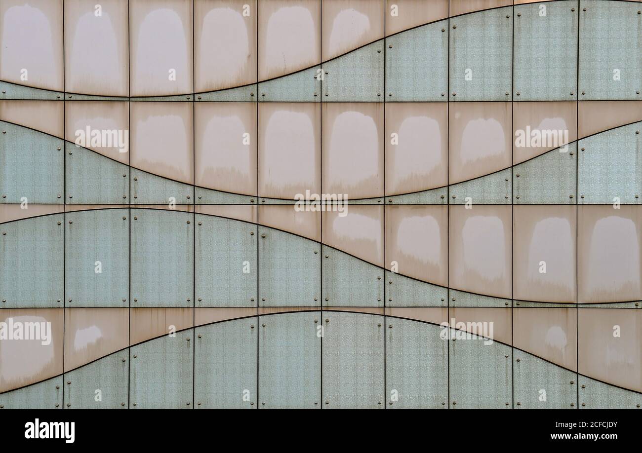 Ein zeitgemäßes modernes Gebäude mit einer futuristischen Fassade aus beigefarbenen und schieferblauen gebogenen, genieteten Glaspaneelen, die einen Welleneffekt erzeugen. Stockfoto