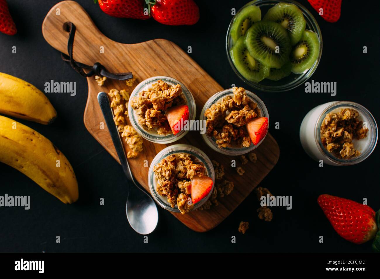 Von oben Anordnung von Bananen, Schüssel in Scheiben geschnitten Kiwi, Milchflaschen mit Walnüssen und Erdbeere auf schwarzem Hintergrund Stockfoto