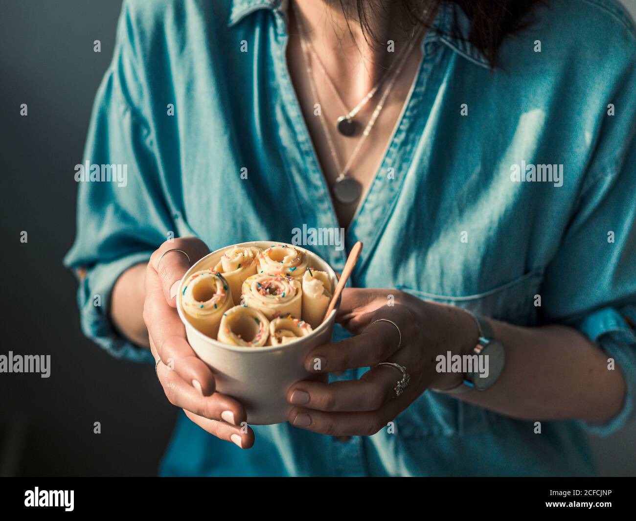 Gerolltes Eis in Kegelbecher in Frauenhänden. Frau in Jeans-Hemd hält Kegelbecher mit thai-Stil Vanille gewalzte Eis Stockfoto