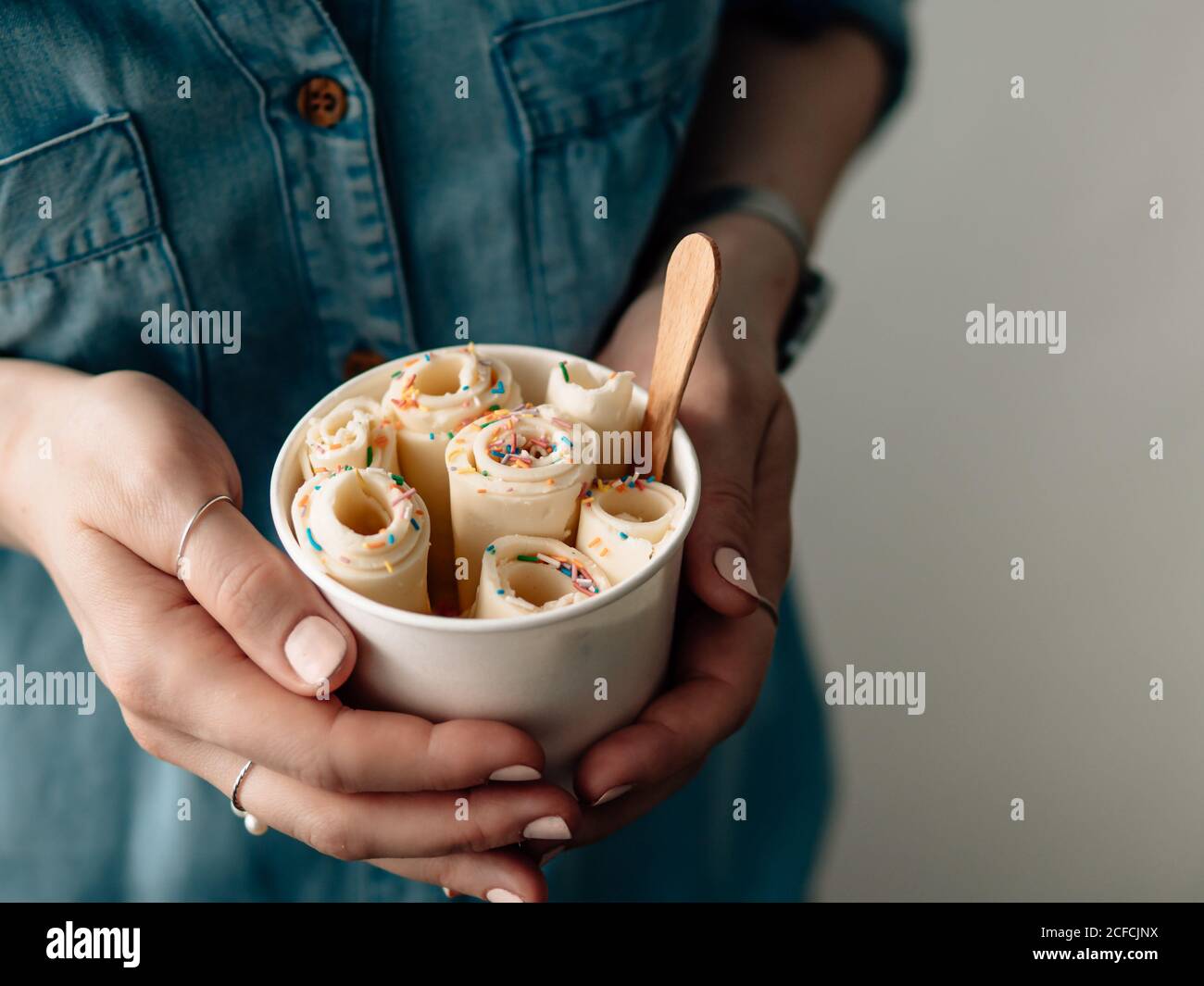 Gerolltes Eis in Kegelbecher in Frauenhänden. Frau in Jeans-Hemd hält Kegelbecher mit thai-Stil Vanille gewalzte Eis Stockfoto