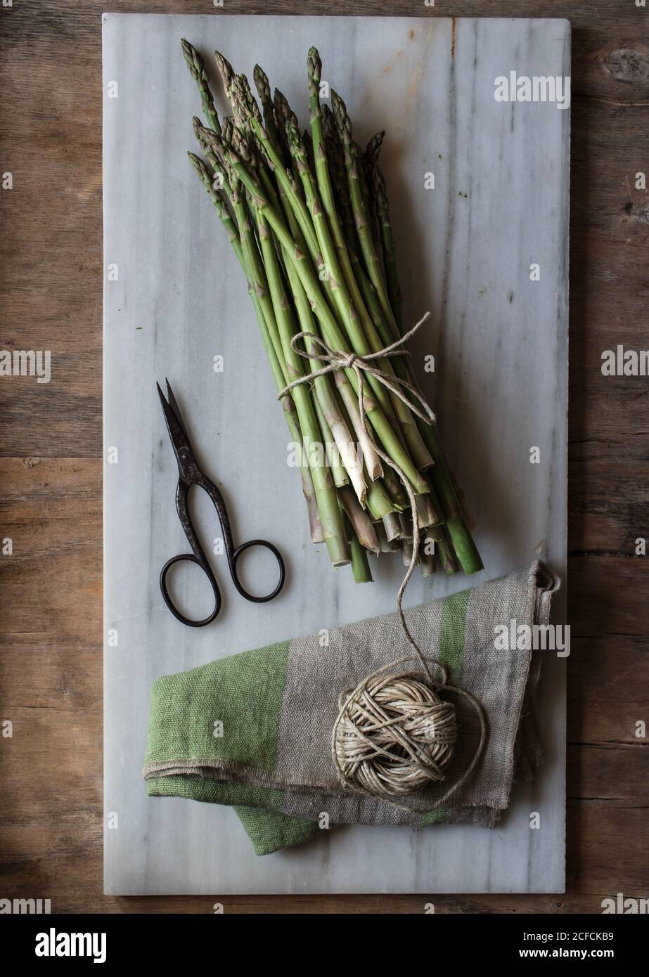 Draufsicht auf Marmorplatte mit Spargelstapel gebunden Mit Kordelzug auf Holztisch Stockfoto