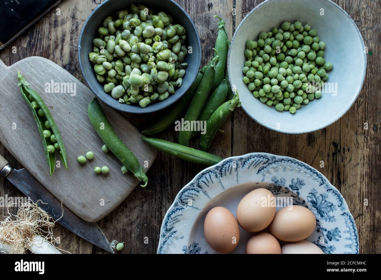 Oben vom Seil frische grüne Erbsen in der Schüssel und Eier auf Holztisch beim Kochen Stockfoto