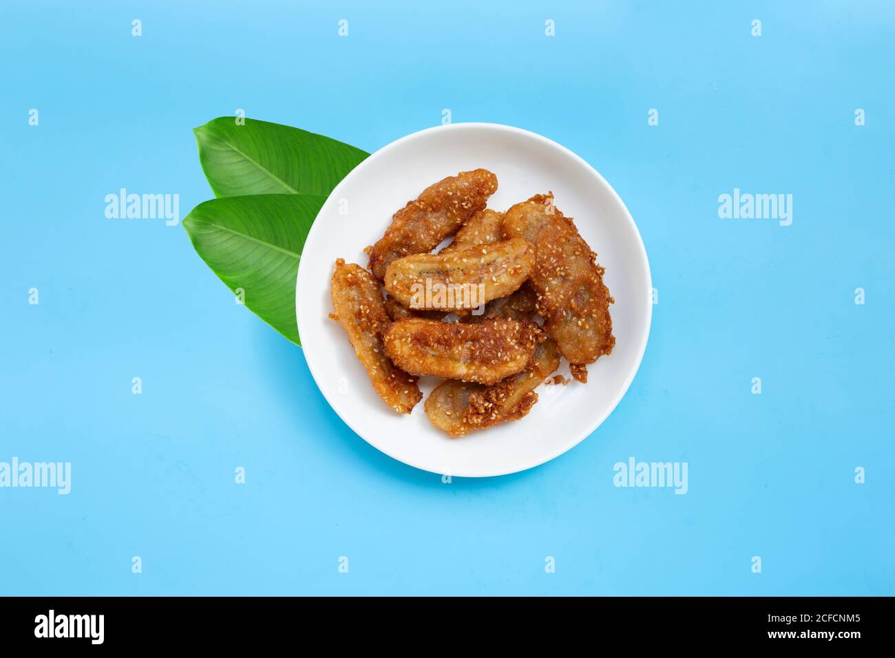 Gebratene Bananen mit Sesam auf weißem Keramik-Rundteller auf blauem ...