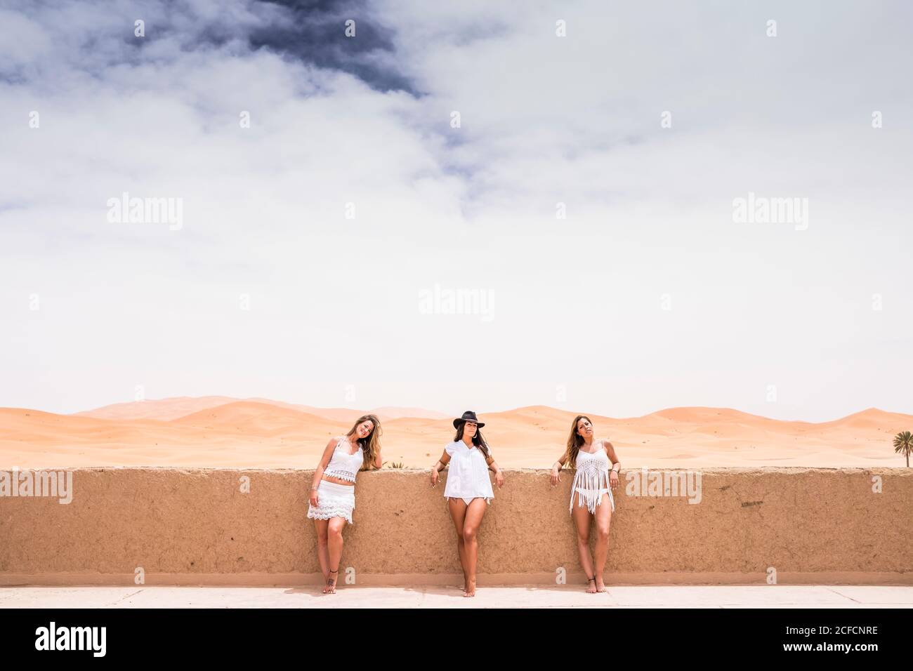 Reihe von Frauen in weißen Strandmode posiert am Steinzaun auf der Terrasse gegen endlose Wüste, Marokko Stockfoto