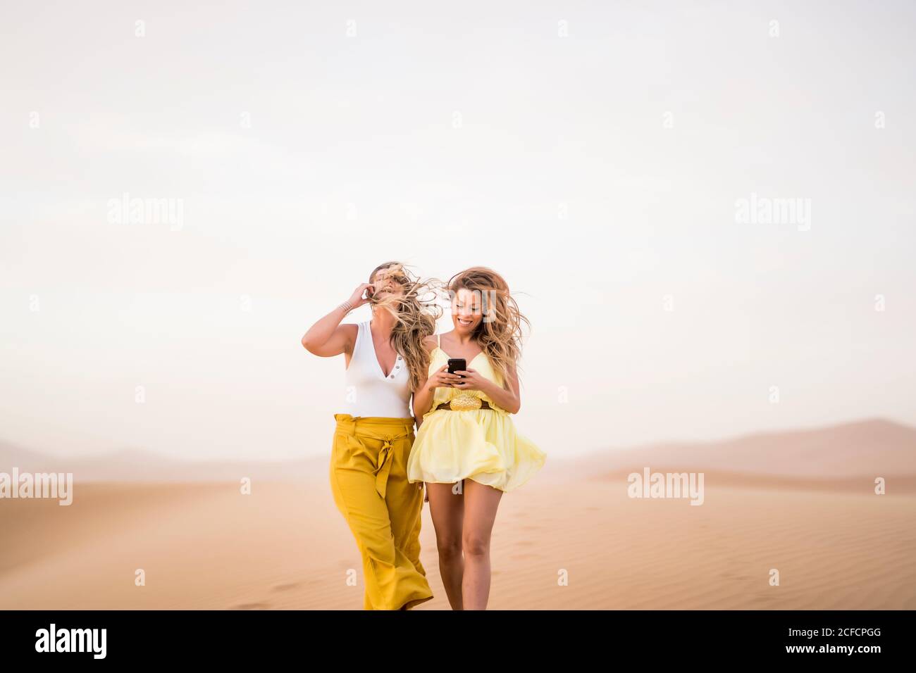 Fröhlich stilvolle zwei blonde Frauen Freunde mit Handy, während Wandern in der Wüste von Marokko Stockfoto