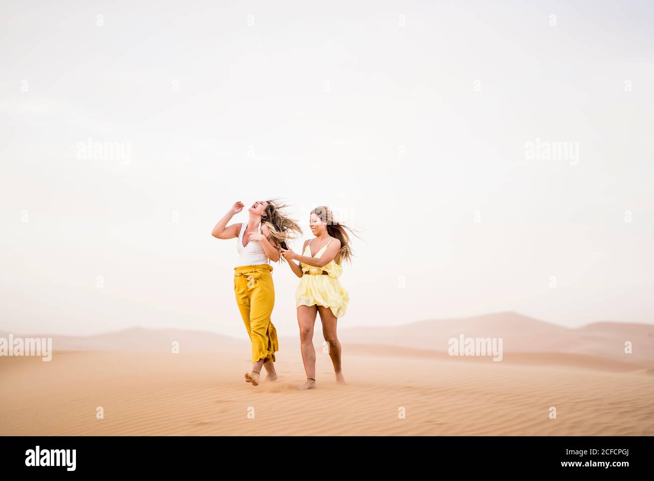 Fröhlich stilvolle zwei blonde Frauen Freunde mit Handy, während Wandern in der Wüste von Marokko Stockfoto