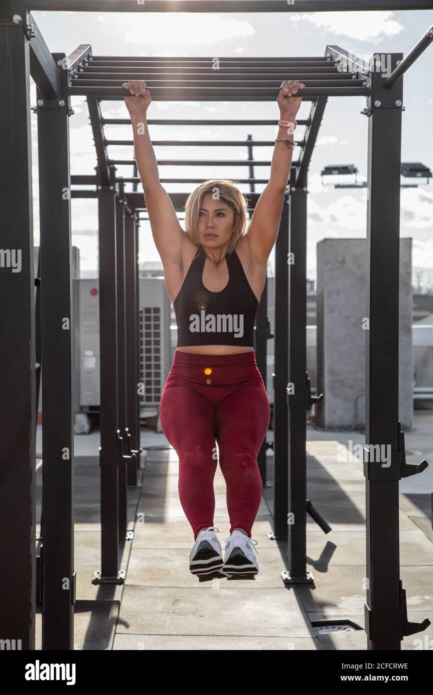 Sportlich blond in stilvoller Active Wear an Bar und hängen Die Beine bis zum Bauch auf dem Dach des Gebäudes zu ziehen Weg Stockfoto