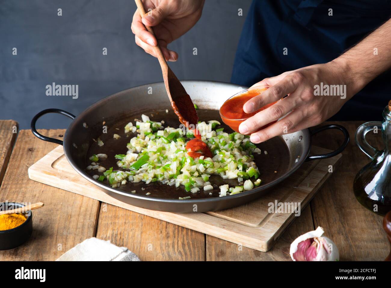Von oben unkenntlich kochen Zugabe von Tomatenmark mit Holzspatel Zu gehackter grüner Chilischote und Zwiebel auf groß gemischt Metallpfanne während der Zubereitung der Zutaten in der modernen Küche Zu Hause Stockfoto