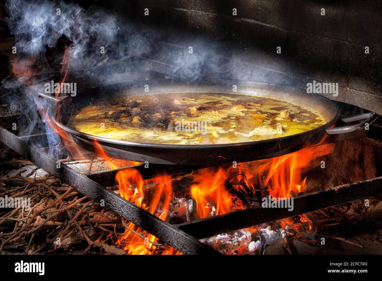 Große Eisenpfanne mit kochender Brühe zum Kochen von Paella Offenes Feuer mit Holz Stockfoto
