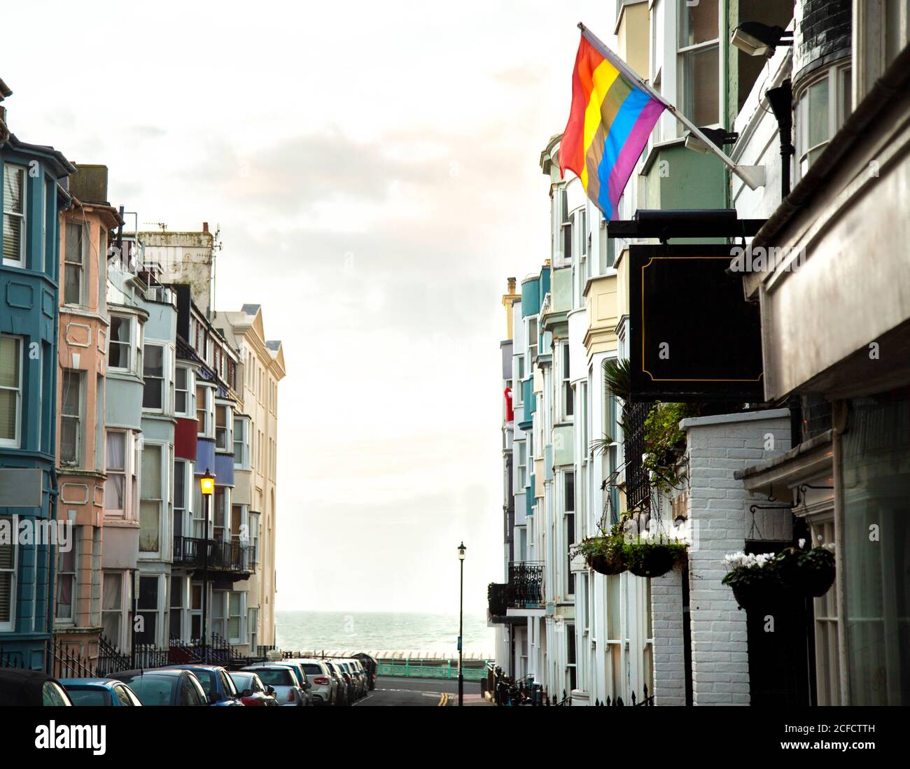 Helle Regenbogenfahne, die LGBT-Bewegung symbolisiert und an der Fassade hängt Eines alten Wohnhauses in der Straße von Brighton in der Nähe des Meeres Stockfoto