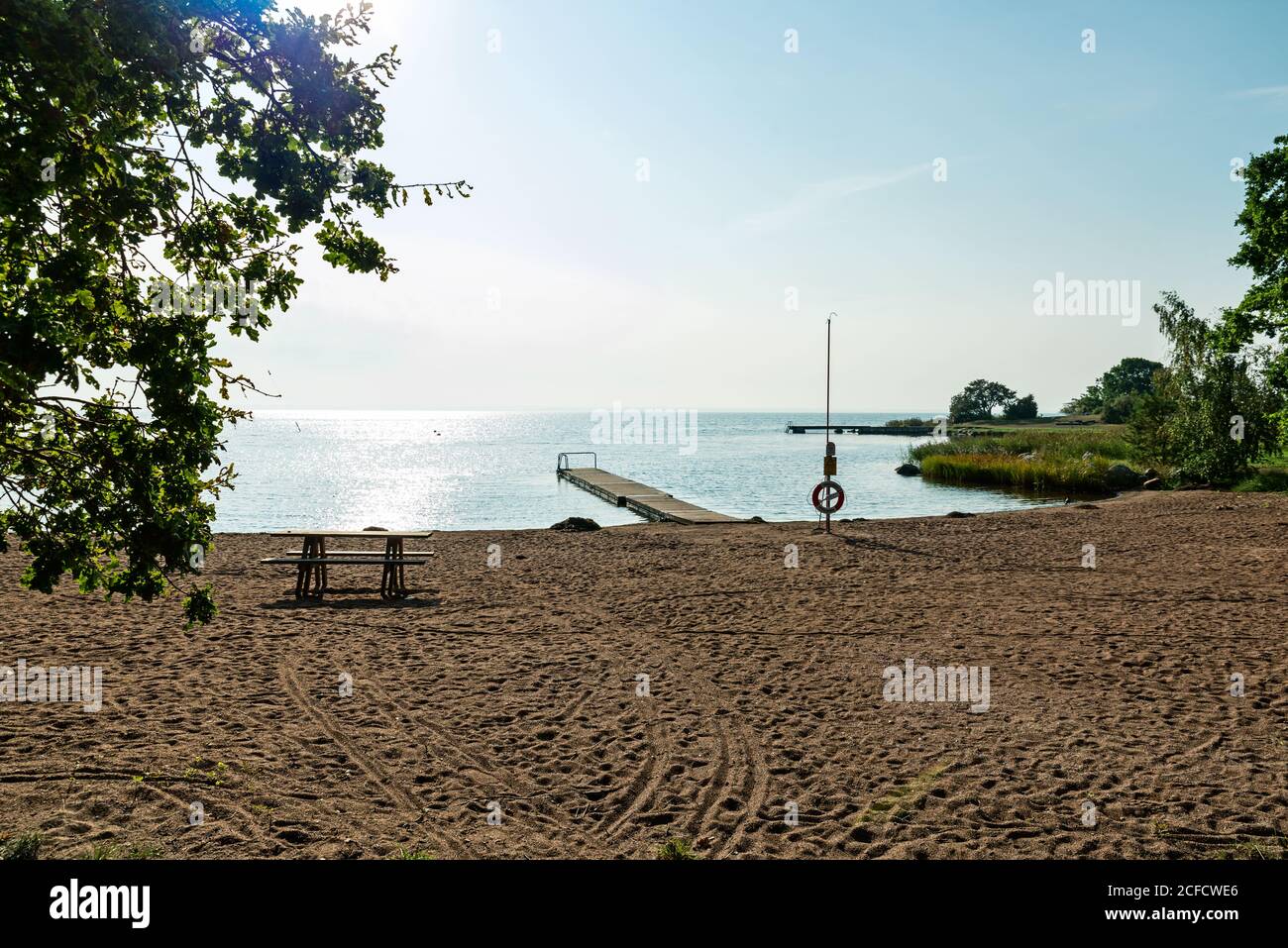 Sandstrand mit Bank, Steg und Rettungsring, eingerahmt von Grün Stockfoto