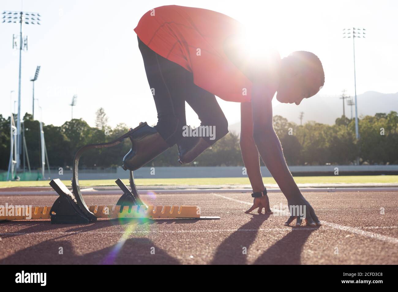 Männlicher Athlet mit prothetischen Beinen, die sich vor dem Startblock biegen Das Rennen Stockfoto