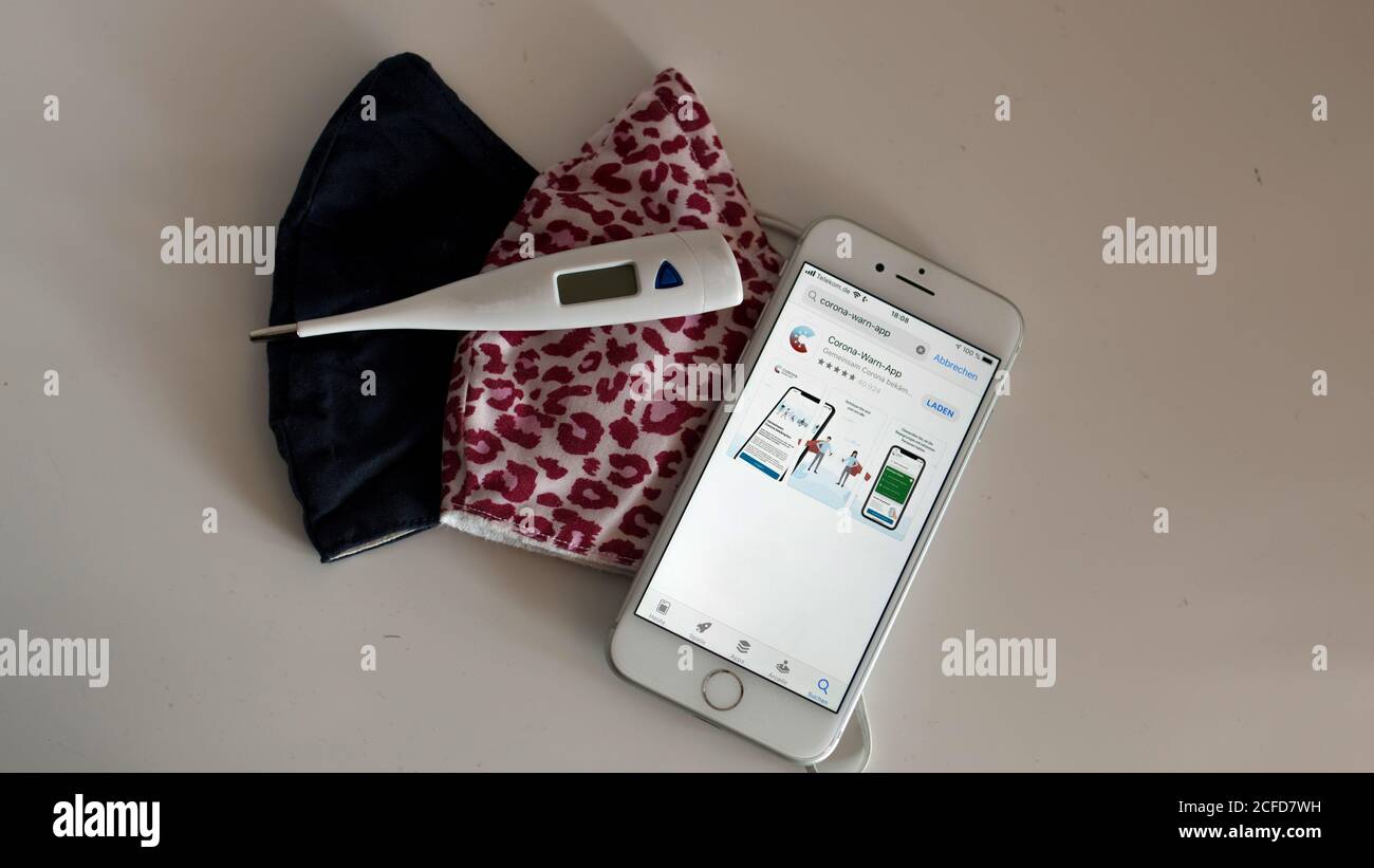 Corona Warnung App auf dem iphone und Mund-Nase Maske auf dem Tisch Mit klinischem Thermometer Stockfoto