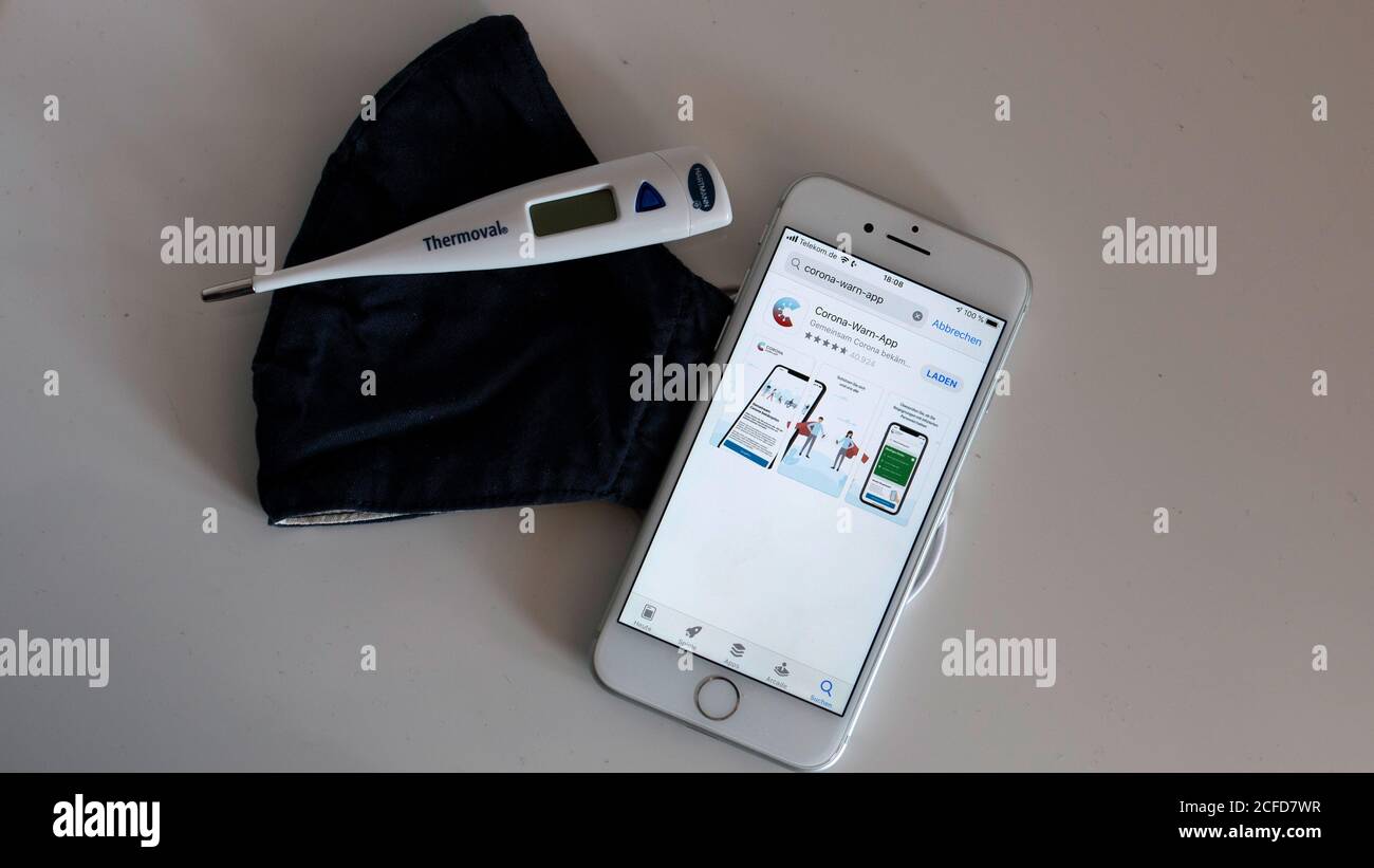 Corona Warnung App auf dem iphone und Mund-Nase Maske auf dem Tisch Mit klinischem Thermometer Stockfoto