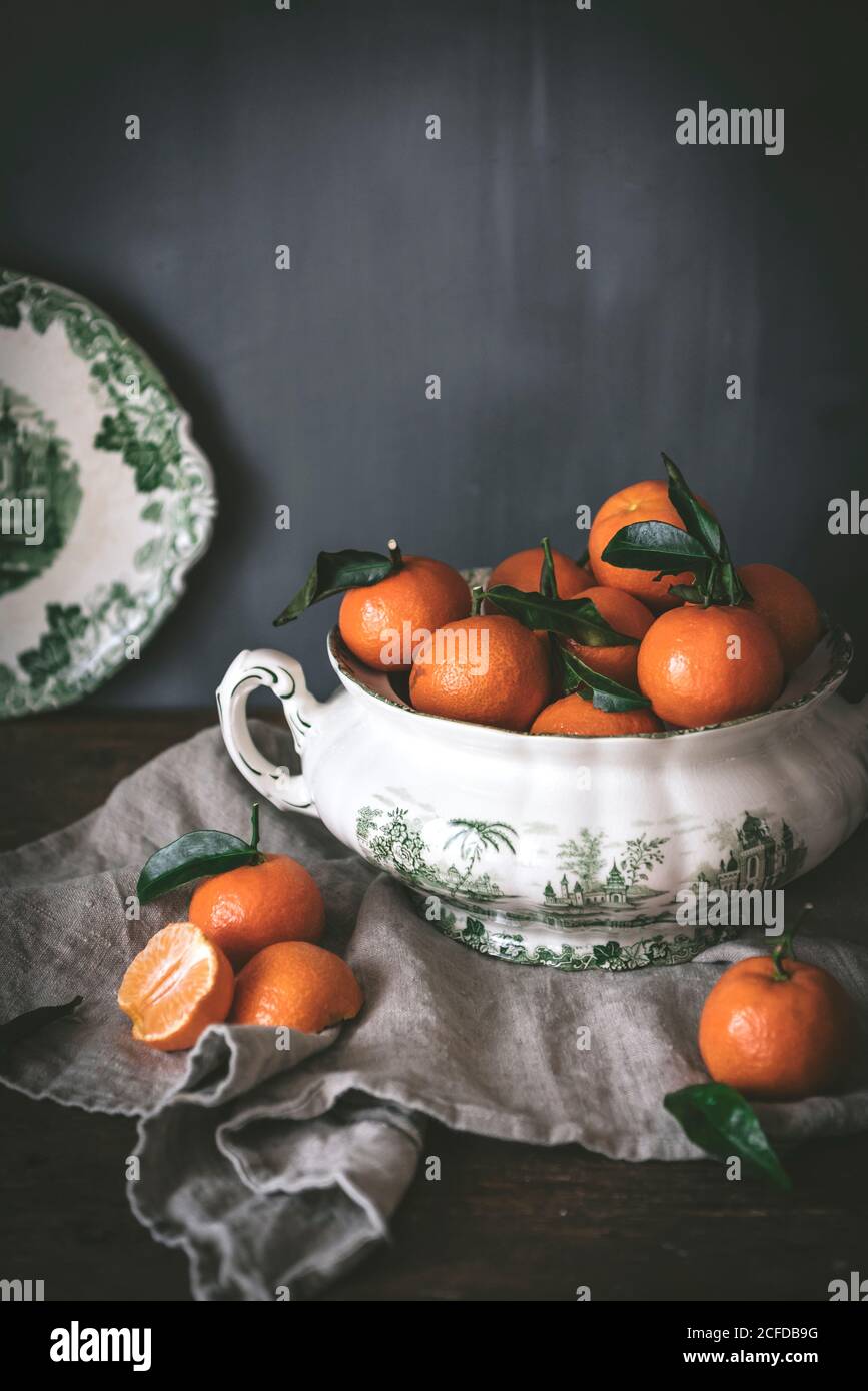 Anspruchsvolles Stillleben mit reifen orangen Mandarinen mit grünen Blättern In tiefweißer Schale auf Tisch auf grauem Hintergrund Stockfoto
