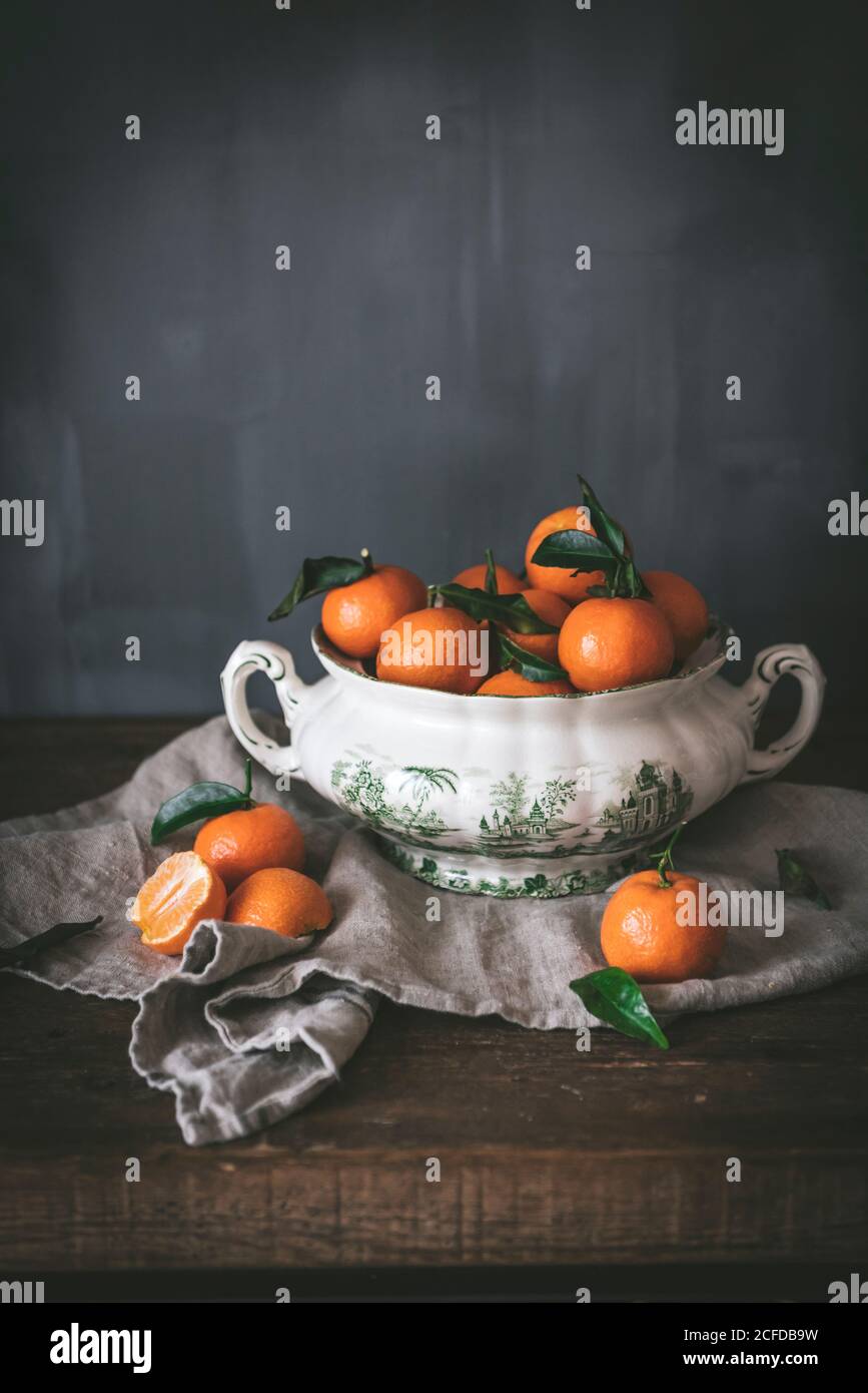 Anspruchsvolles Stillleben mit reifen orangen Mandarinen mit grünen Blättern In tiefweißer Schale auf Tisch auf grauem Hintergrund Stockfoto
