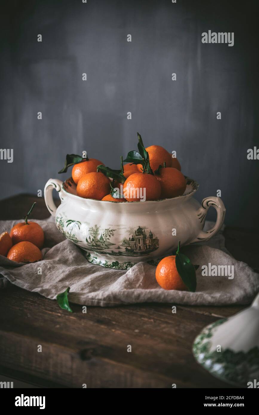 Anspruchsvolles Stillleben mit reifen orangen Mandarinen mit grünen Blättern In tiefweißer Schale auf Tisch auf grauem Hintergrund Stockfoto