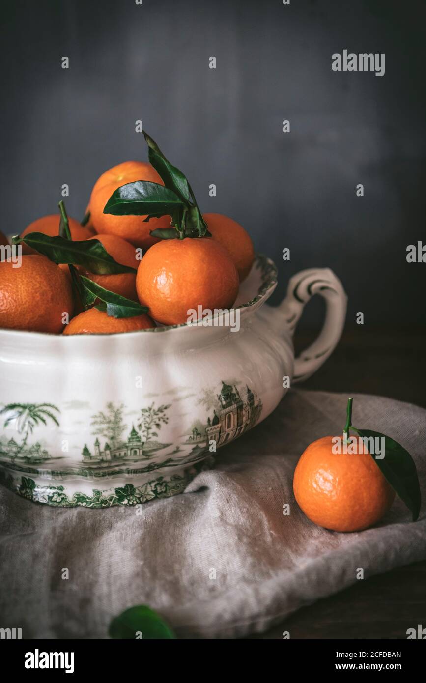 Anspruchsvolles Stillleben mit reifen orangen Mandarinen mit grünen Blättern In tiefweißer Schale auf Tisch auf grauem Hintergrund Stockfoto