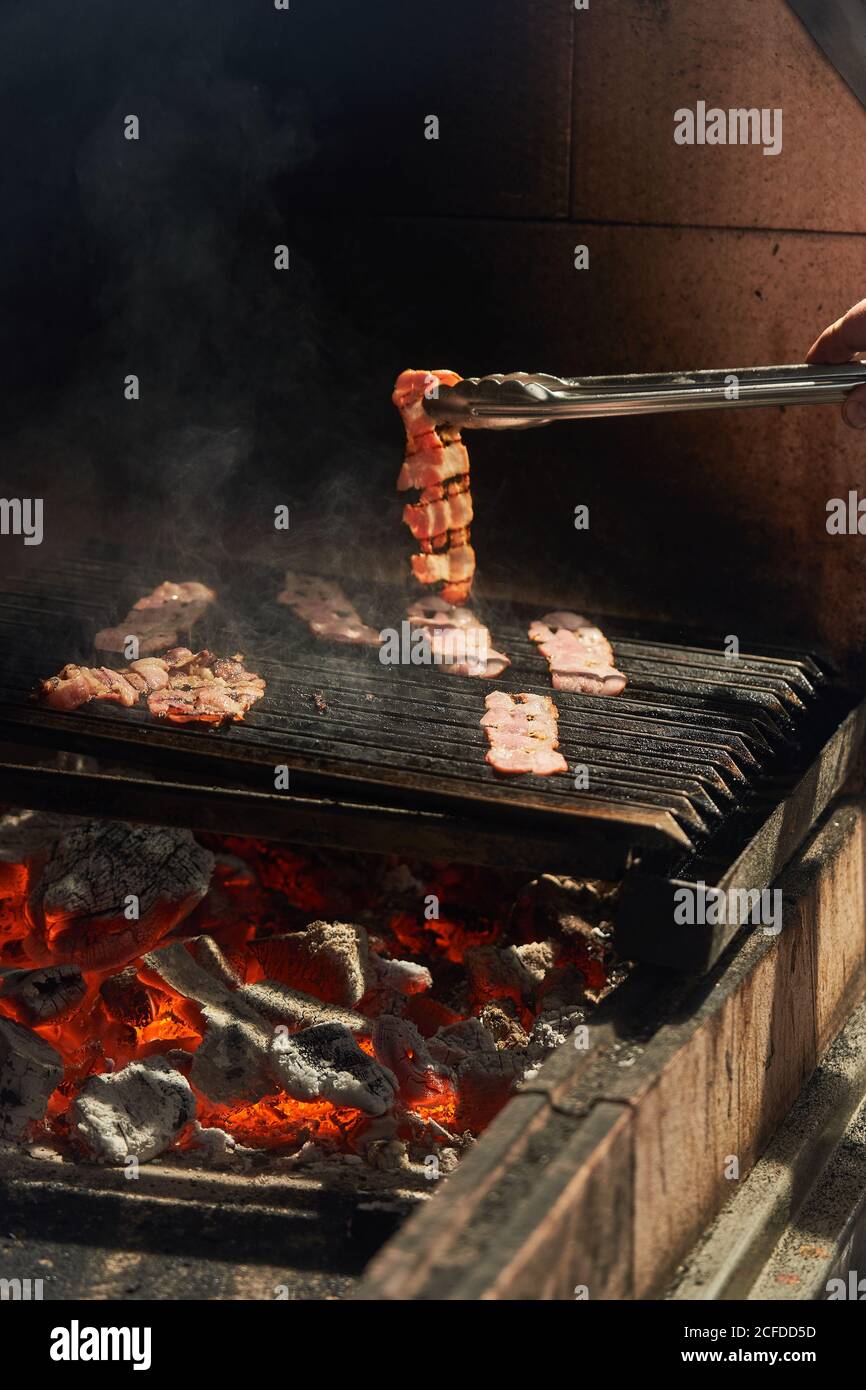 Crop Chef Drehen Riemen des Grillens saftigen Speck während des Kochens Mit Rauch auf Regal im Garten Stockfoto