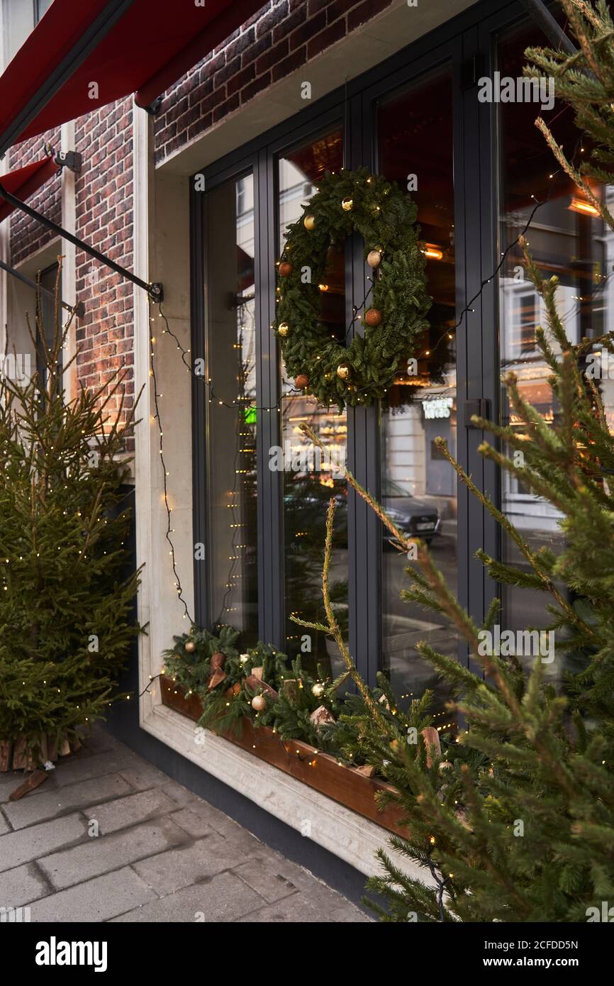 Fassade des Cafés mit bunten Dekorationen von Nadelbäumen und Weihnachtsbaum mit Girlanden bei Tageslicht Stockfoto