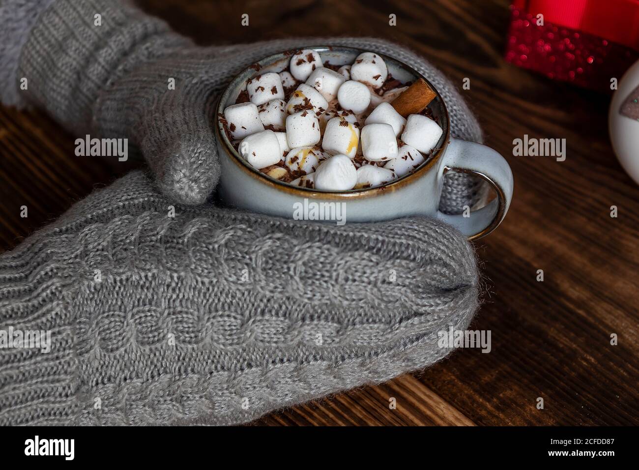 Gemütliche Feiertagskomposition, Hände in Fäustlingen halten Becher mit Kakao oder Schokolade mit Marshmallow. Stockfoto