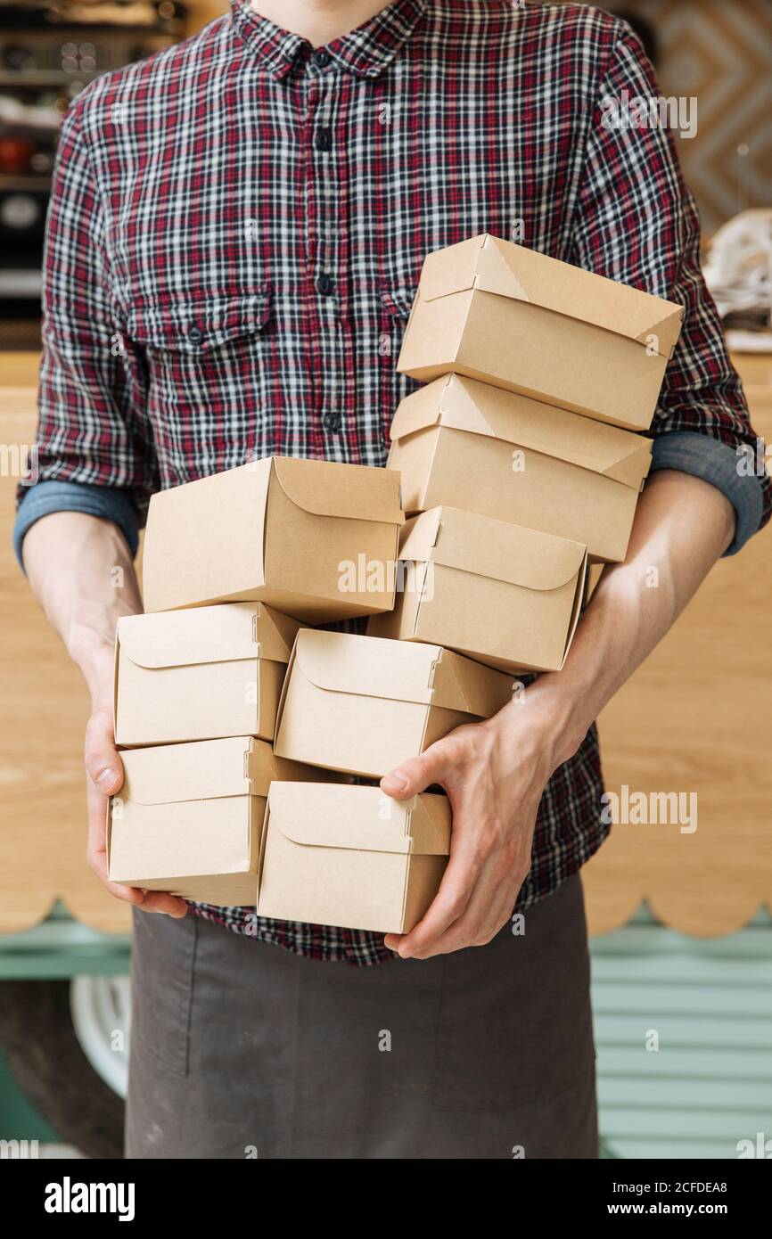 Unkenntlich Mann in kariertem Hemd mit viel kleiner Pappe Boxen mit gelieferten Speisen im Restaurant Stockfoto