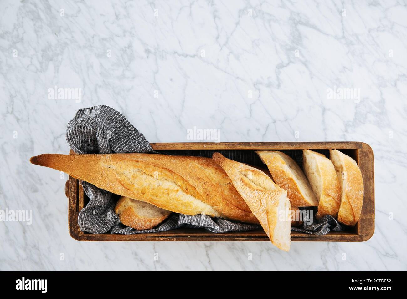 Blick von oben auf köstliche frisch geschnittene Baguette auf Holz serviert Tablett auf Marmortisch platziert Stockfoto