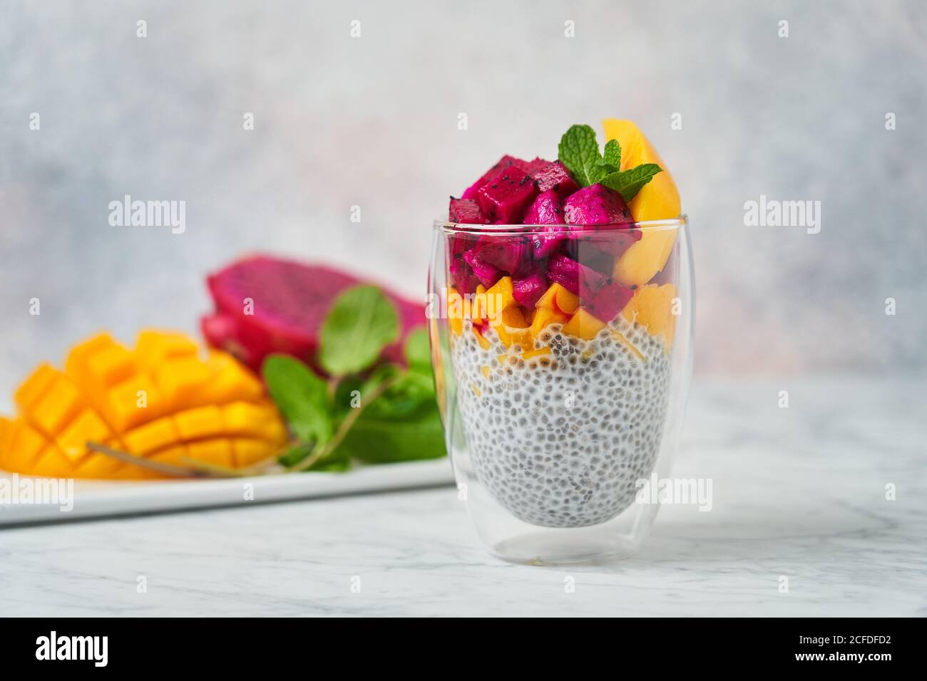 Chia Pudding mit Scheiben von Mango roten Pitaya und dekoriert Frische Minze im Glas mit frischen Zutaten auf verschwommenem Hintergrund Stockfoto
