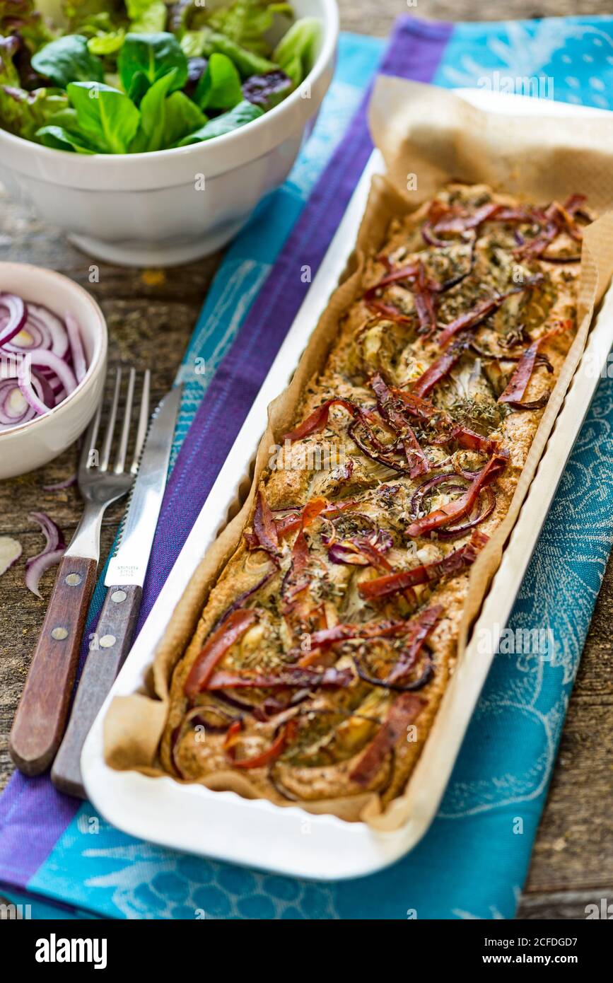 Foccacia frisch aus dem Ofen, in einer rechteckigen Tartpfanne, mit grünem Salat, extra roten Zwiebeln und Artischocken Stockfoto