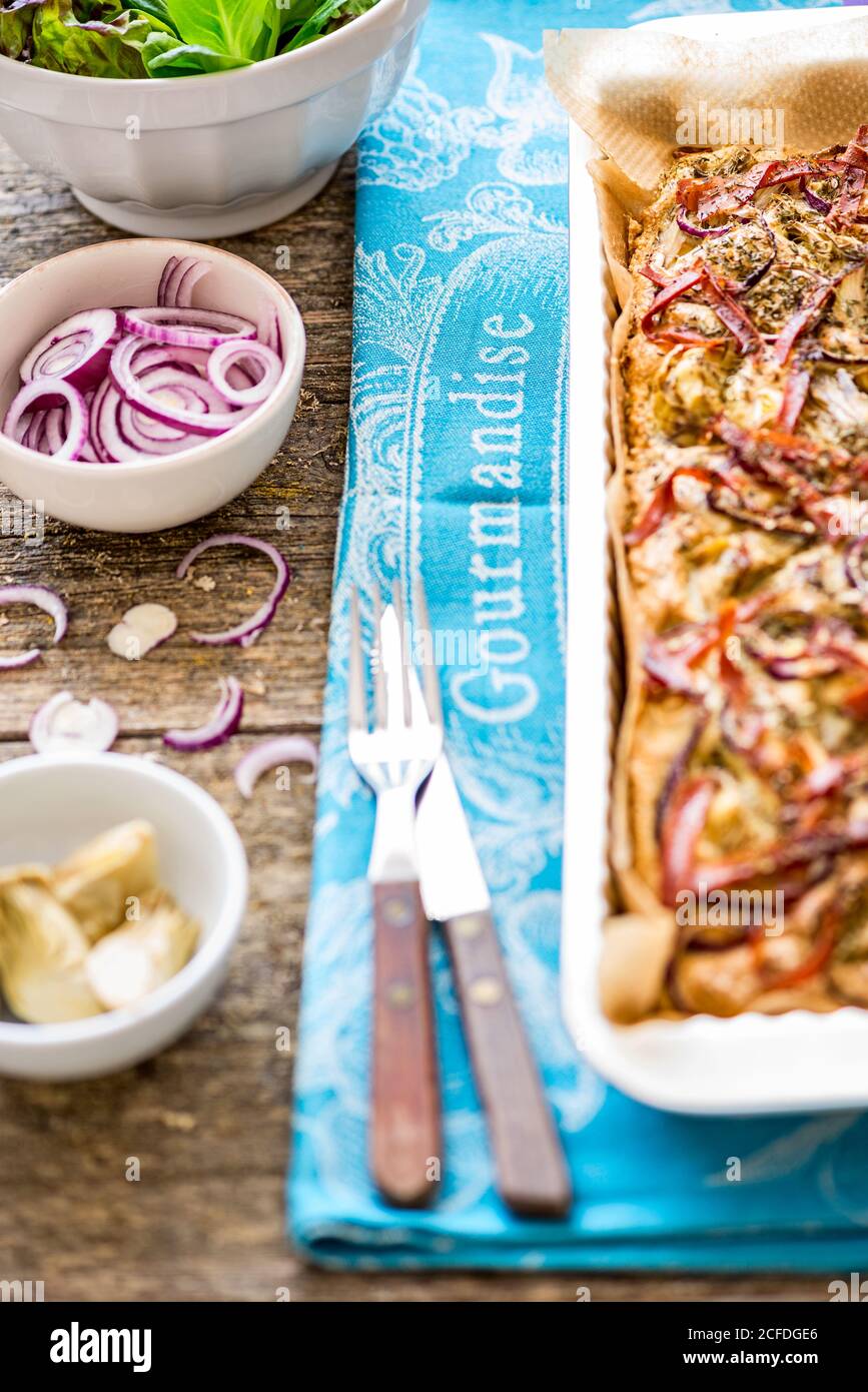 Foccacia frisch aus dem Ofen, in einer rechteckigen Tartpfanne, mit grünem Salat, extra roten Zwiebeln und Artischocken Stockfoto