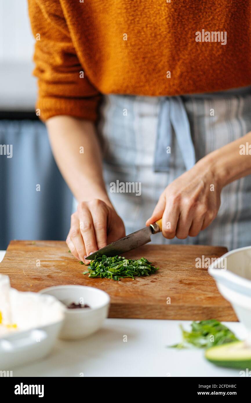 Ernte Hausfrau Schneiden frische grüne Kräuter auf Holzbrett, während Zubereitung von köstlichen Abendessen in der Küche zu Hause Stockfoto