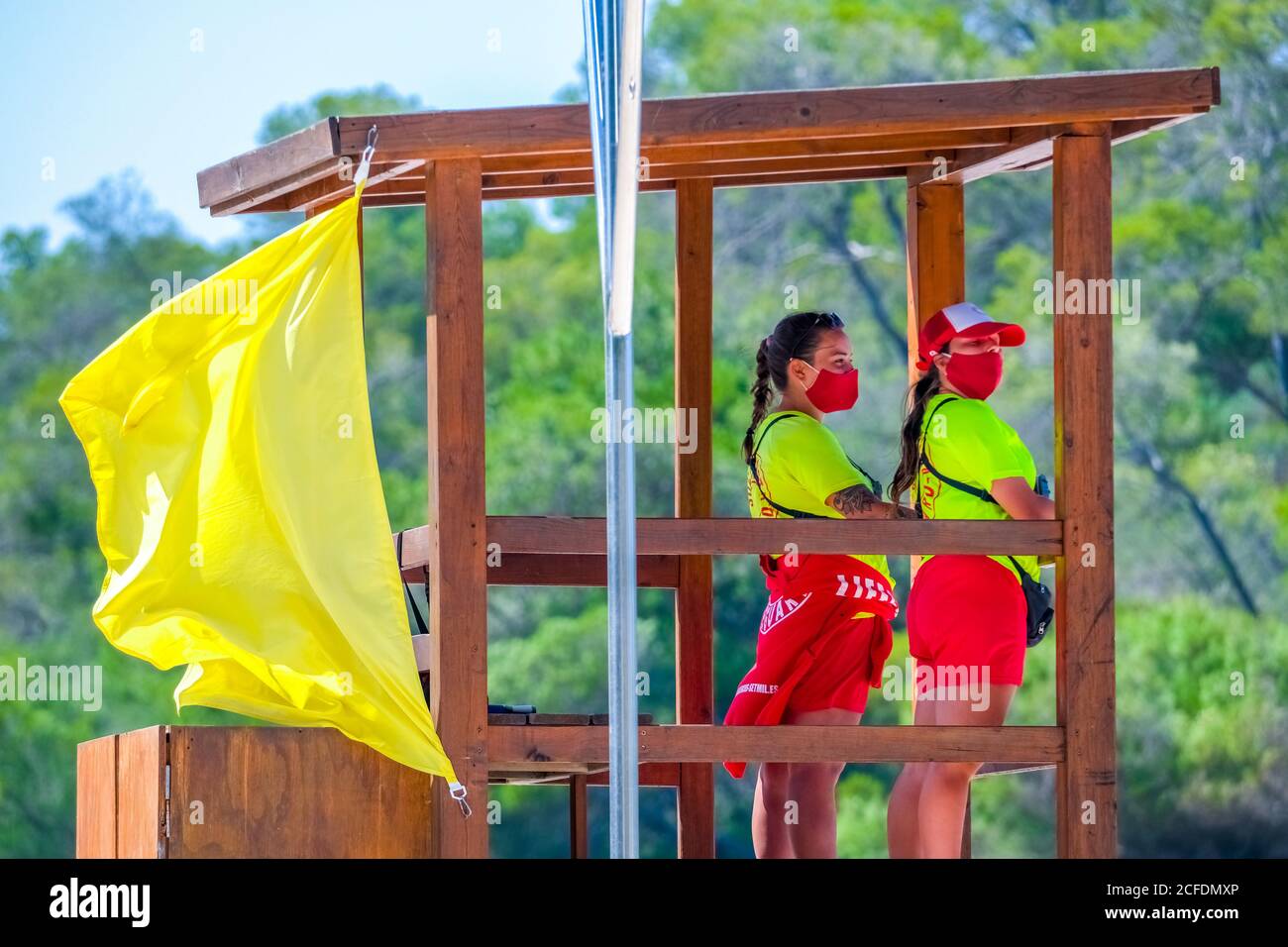 Rettungsschwimmer, Rettungsschwimmer mit Corona-Maske, achten Sie auf die Schwimmer an der orangefarbenen Warnflagge am Strand von S'amador. Abgelegener Badestrand Stockfoto