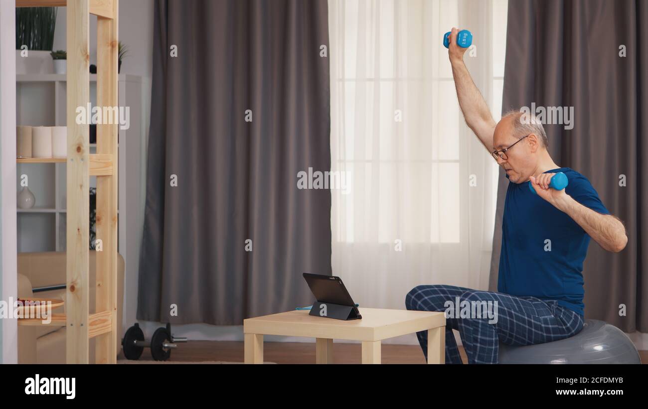 Großvater Training im Wohnzimmer mit Hanteln beobachten Online-Fitness-Programm. Alter Rentner gesundes Training Gesundheit Sport zu Hause, Fitness-Aktivität im Alter ausüben Stockfoto