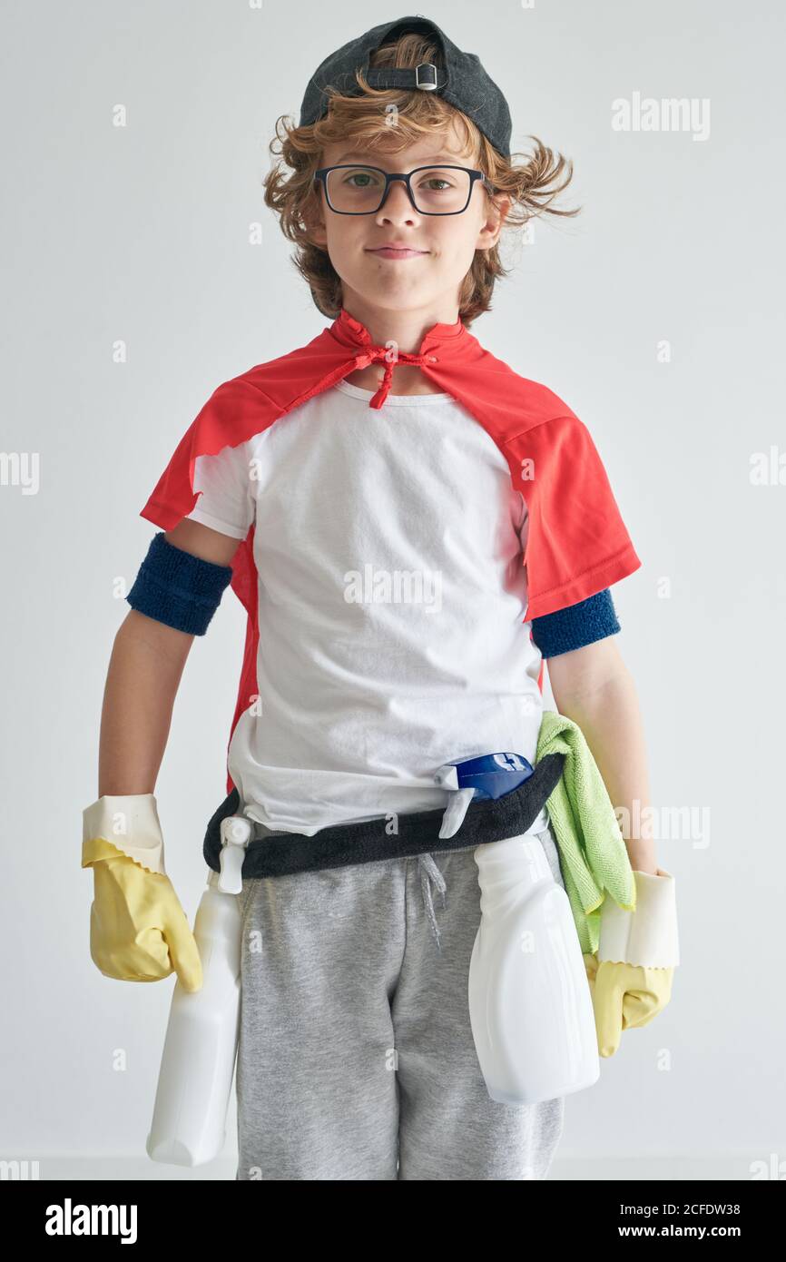 Selbstbewusster Junge in Superhelden Umhang mit Waschmitteln Blick auf die Kamera Vor grauem Hintergrund Stockfoto