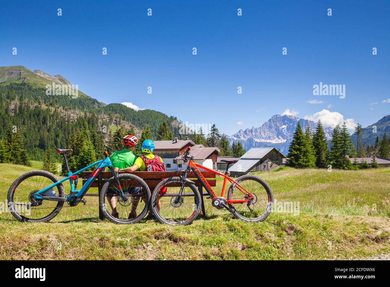 Mann und Frau sitzen auf einer Bank gegenüber dem Civetta Berg bei Cherz alm, Tour mit E-Bike in der Naturlandschaft der Dolomiten, livinallongo del Stockfoto