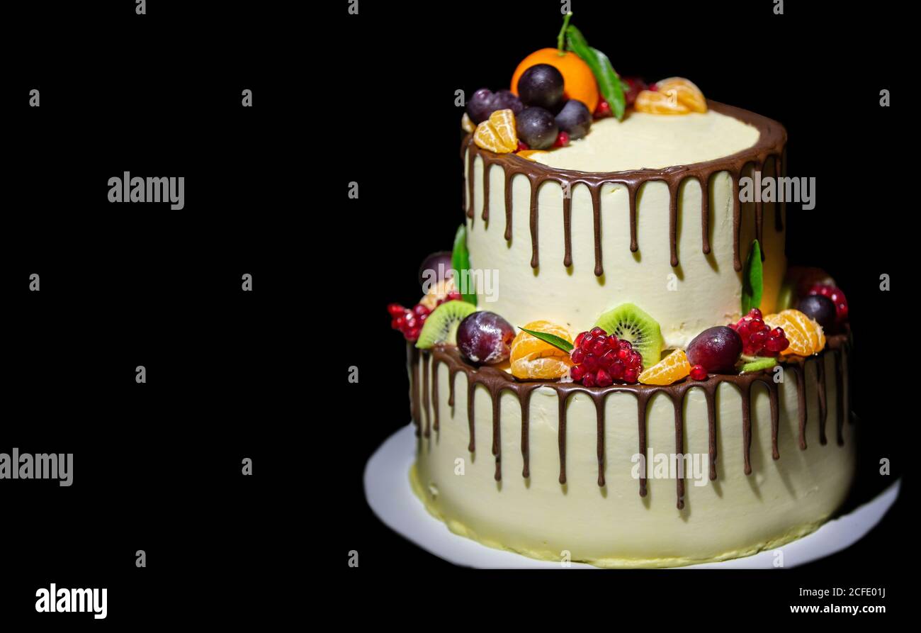 Schöne zweistufige Kuchen mit Schokolade gegossen und mit frischen Früchten auf schwarzem Hintergrund dekoriert. Stockfoto
