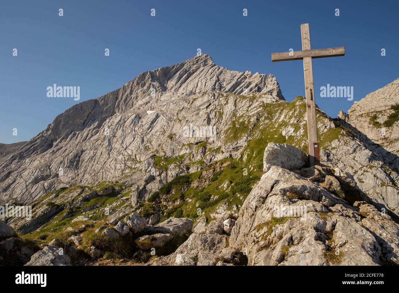 Gipfelkreuz am Osterfelderkopf gegen Alpspitze bei Sonnenaufgang, blauer Himmel, Felsen, Garmisch-Partenkirchen, Oberbayern, Bayern, Süddeutschland, Stockfoto