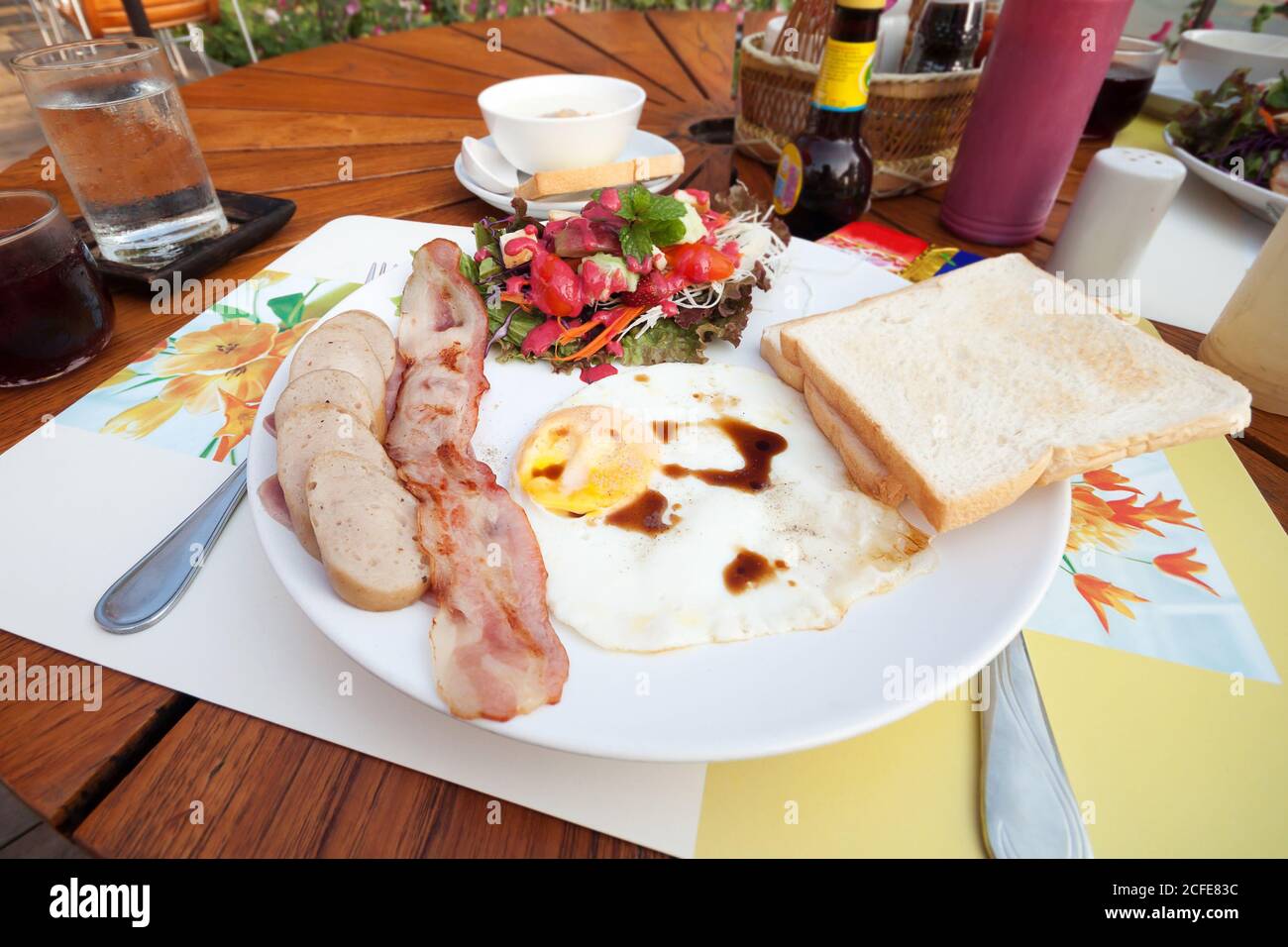 Englisches Frühstück mit Spiegeleiern, Speck, Würstchen, Toast und frischem Salat Stockfoto
