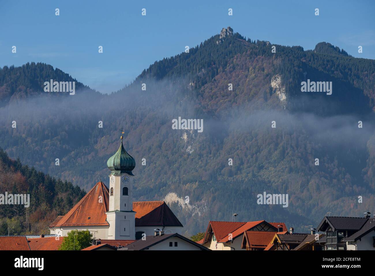 Pfarrkirche St. Clemens in Eschenlohe im Herbst gegen Ettaler Manndl (Ammergauer Alpen), Nebel, blauer Himmel, Bäume, Garmisch-Partenkirchen, Obere Stockfoto
