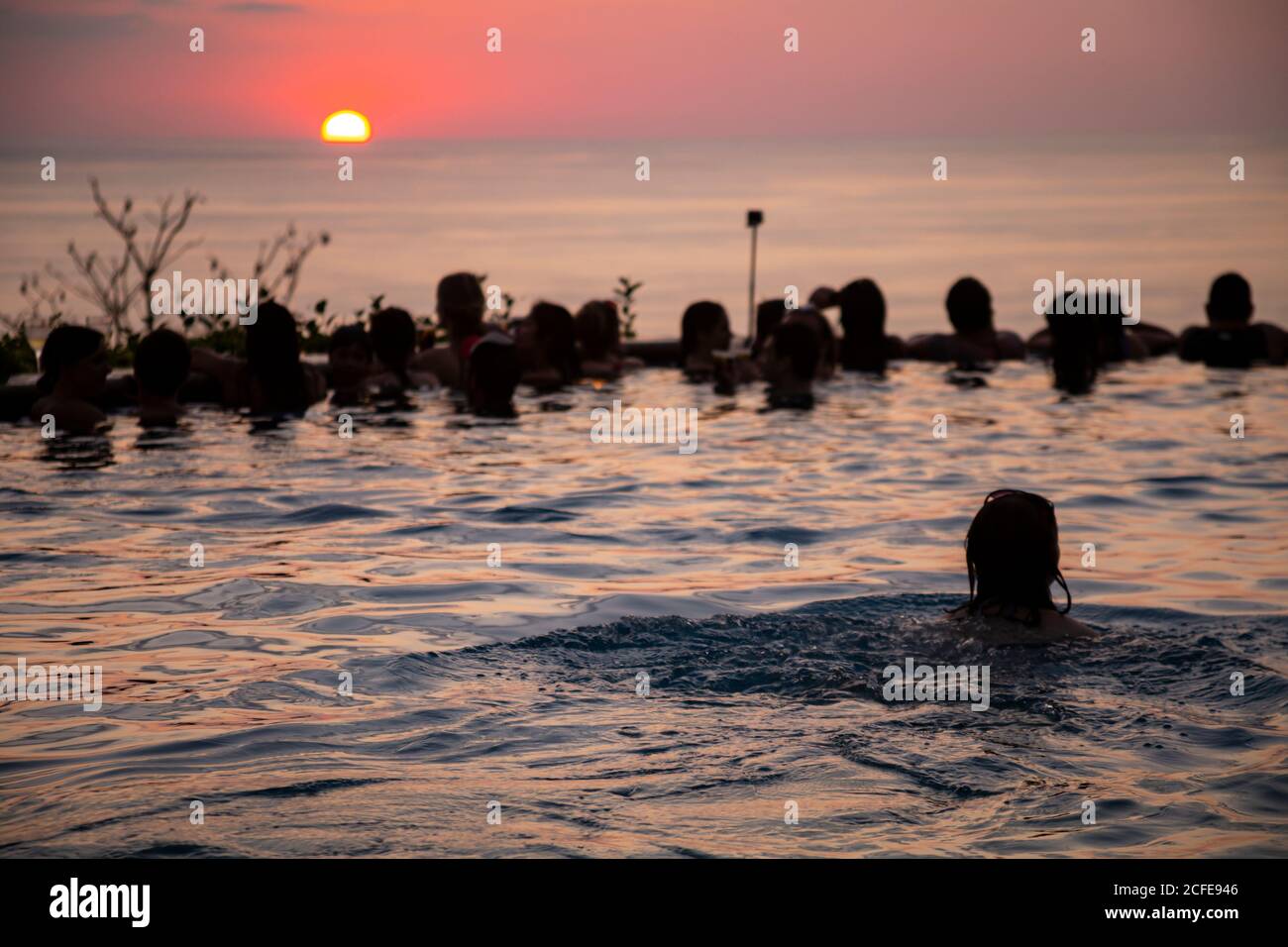 Junge Frau schwimmt im Infinity-Pool, Pool-Party, Sonnenuntergang, Sonne, Silhouette, Meer, junge Frauen, junge Männer, Mittelamerika, Costa Rica Stockfoto