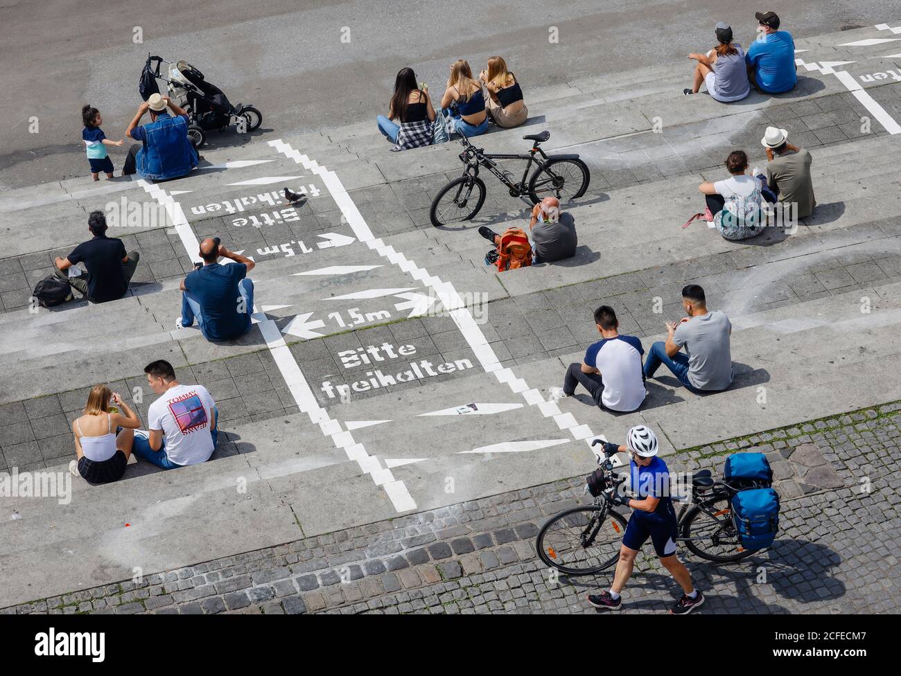 Düsseldorf, Nordrhein-Westfalen, Deutschland - Rheinpromenade in Zeiten der Coronapandemie sitzen Menschen neben gemalten Linien für soziale Distanz Stockfoto
