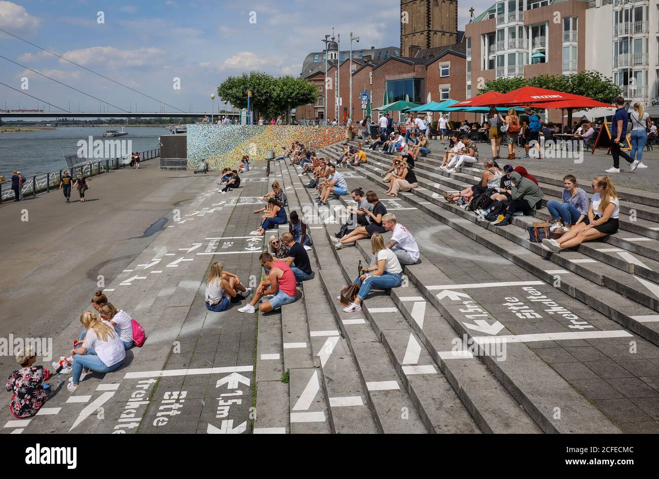 Düsseldorf, Nordrhein-Westfalen, Deutschland - Rheinpromenade in Zeiten der Coronapandemie sitzen Menschen neben gemalten Linien für soziale Distanz Stockfoto