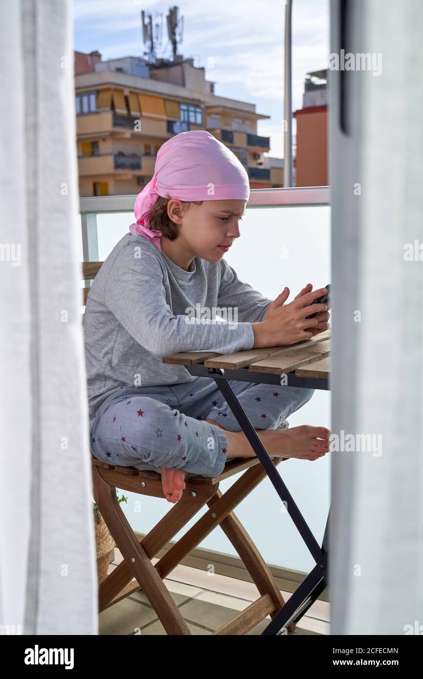 Fröhliches kleines Kind mit Krebserkrankung genießen Zeitvertreib mit Handy Auf der Terrasse Stockfoto