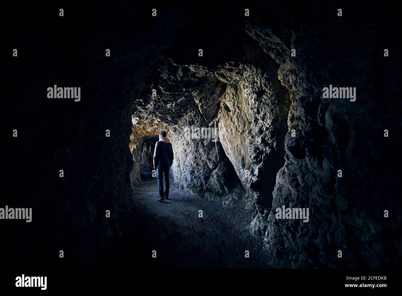 Der junge Mann schaut ins Licht am Ende des Tunnels. Junger Wanderer, der durch einen Tunnel in Felsen geht. Stockfoto