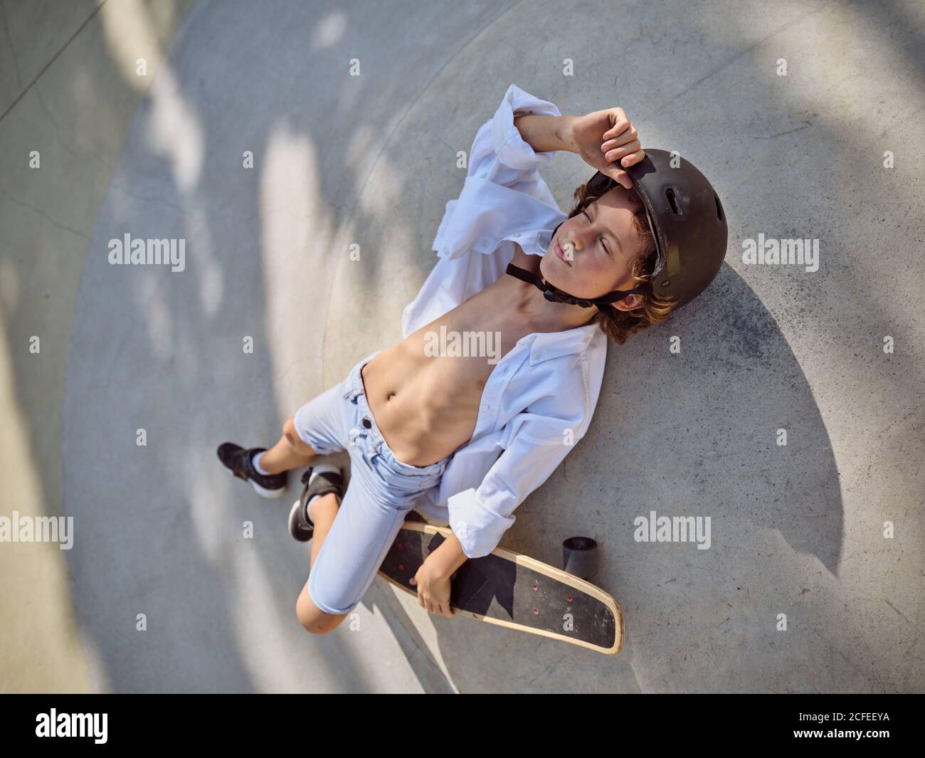 Blick von oben auf Kind im Helm liegend mit Augen geschlossen und chillen auf dem Boden im Skatepark mit Schatten Stockfoto