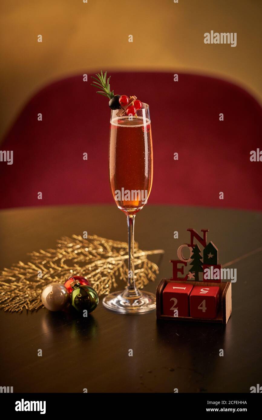 Glas roten Cocktail mit Beeren und grünen Kräutern dekoriert Platziert auf schwarzer Oberfläche mit grünem und goldenem Lametta und Weihnachtskugeln vor verschwommenem Gold Hintergrund Stockfoto