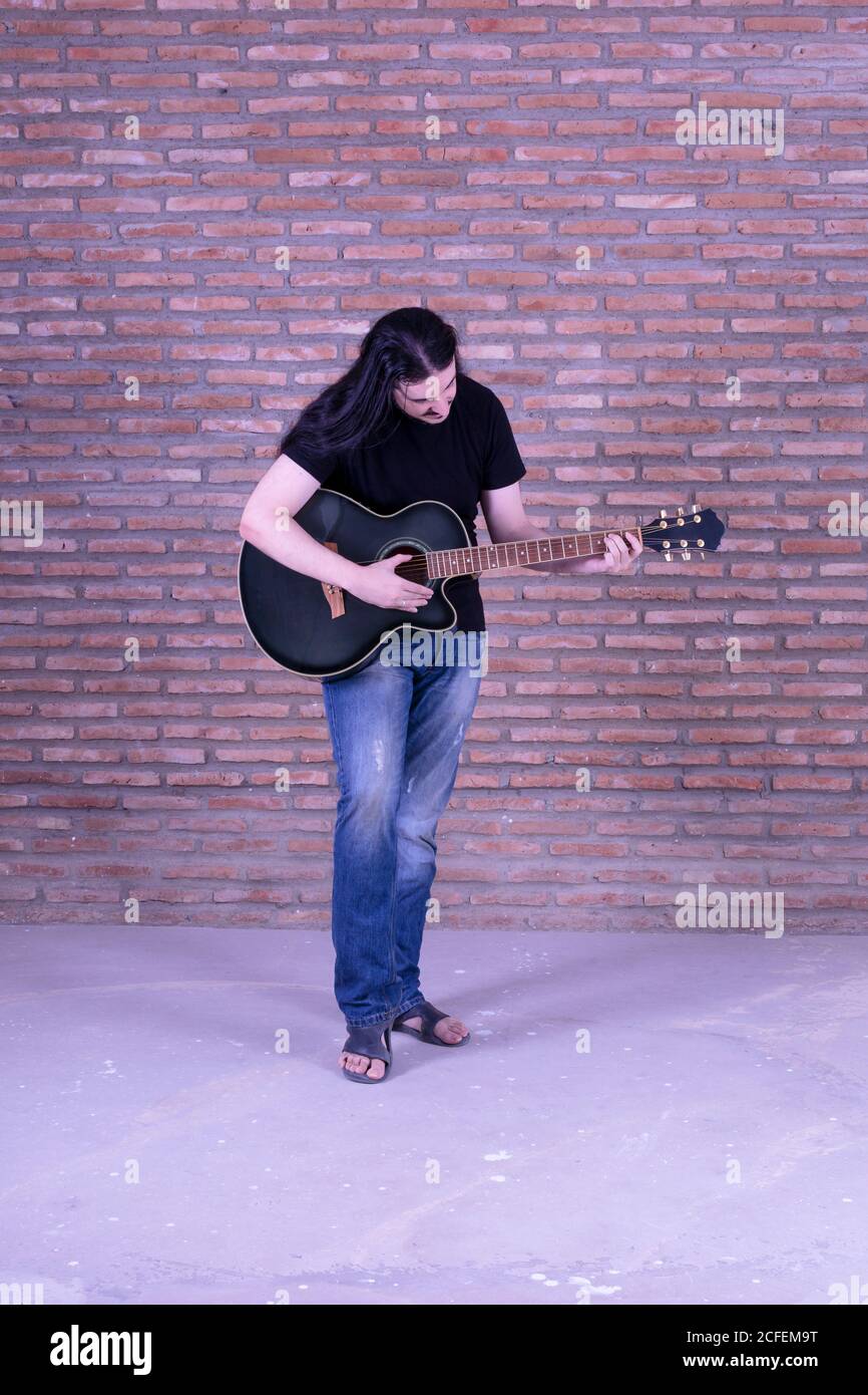 Junger männlicher Gitarrist, der in lässiger Kleidung spielt Stockfoto