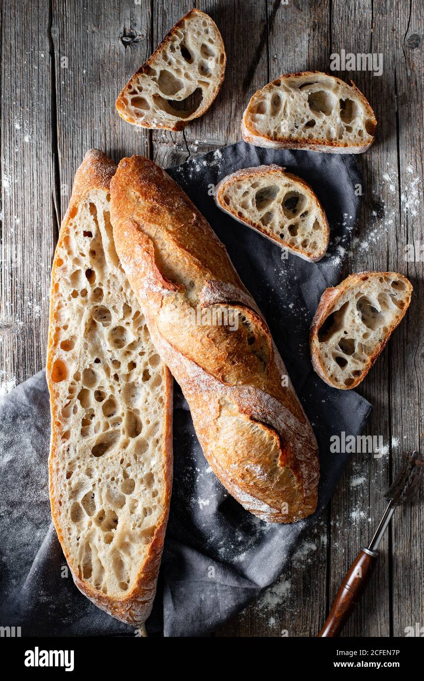 Von oben ganze und halbierte appetitliche Baguettes auf Weiß angeordnet Handtuch vor rustikalem Holzhintergrund Stockfoto