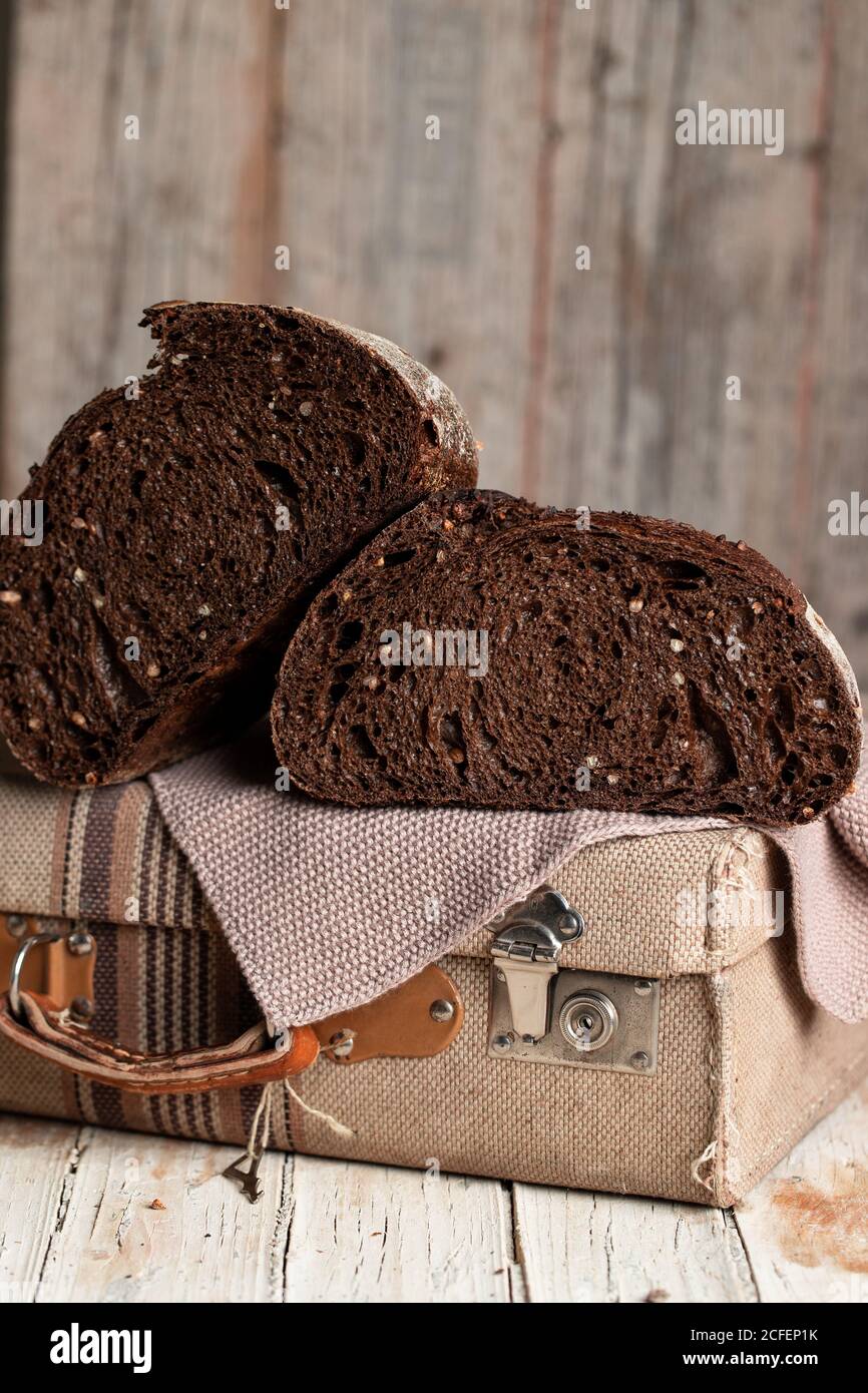 Appetitlich gesunder dunkler Roggenbrotkuchen mit eingeschnitten Körnern Halb auf Retro-Stoffkoffer auf schäbigen Holztisch gelegt Stockfoto